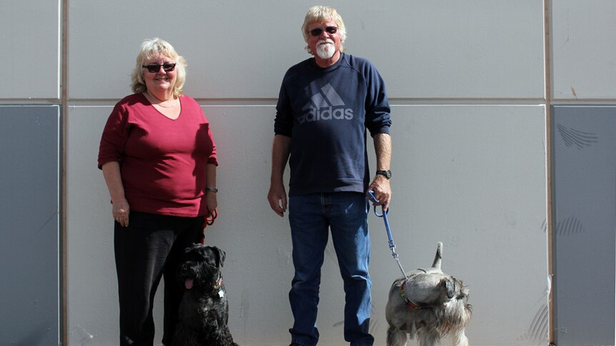 A woman and man with their two dogs standing in front of a bare wall.