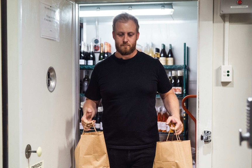 A man walks out of a storeroom carring two brown paper bags.