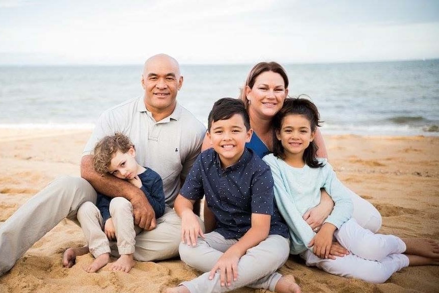 Jodie Elisara sits on a beach with her husband and three children.