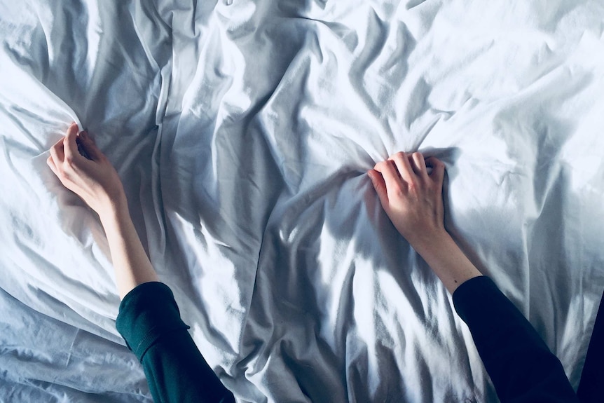 A woman holds a white bedspread.