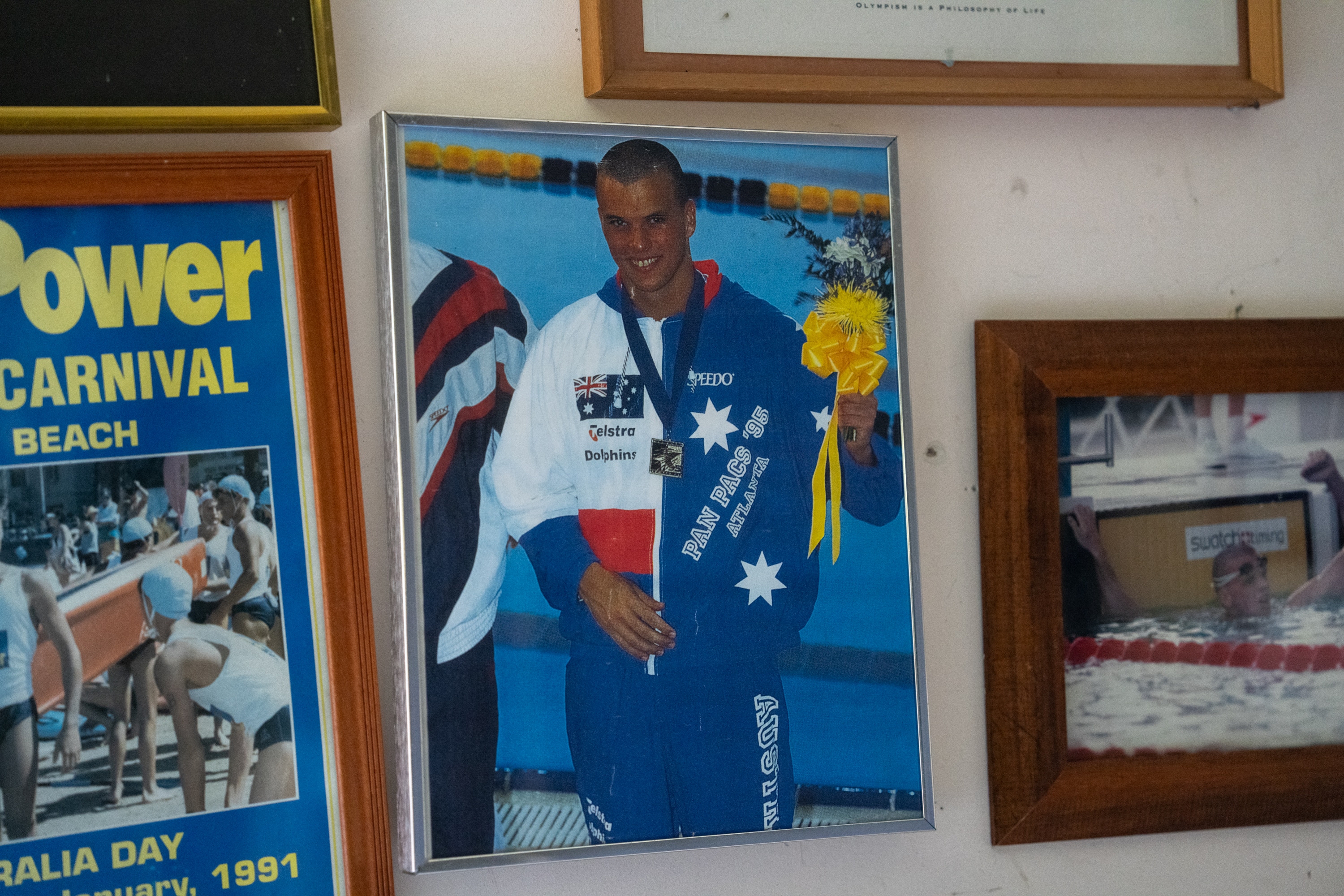 A framed photo of a man wearing an Australian flag tracksuit with a gold medal around his neck in front of a swimming pool.