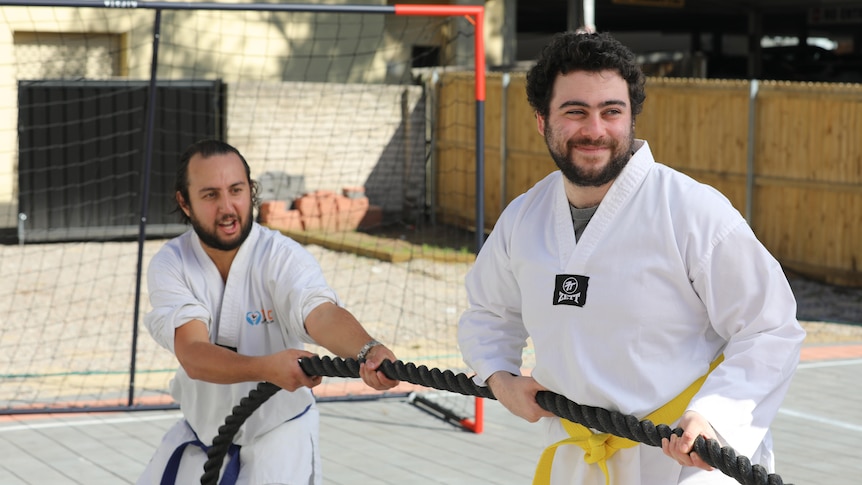 Two men with smiling faces wearing white martial arts uniforms and pulling a rope in a game of tug-o-war.