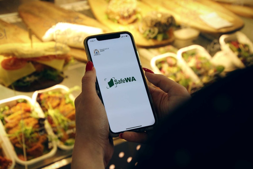 A woman uses the SafeWA app on an iPhone at a cafe in East Perth.