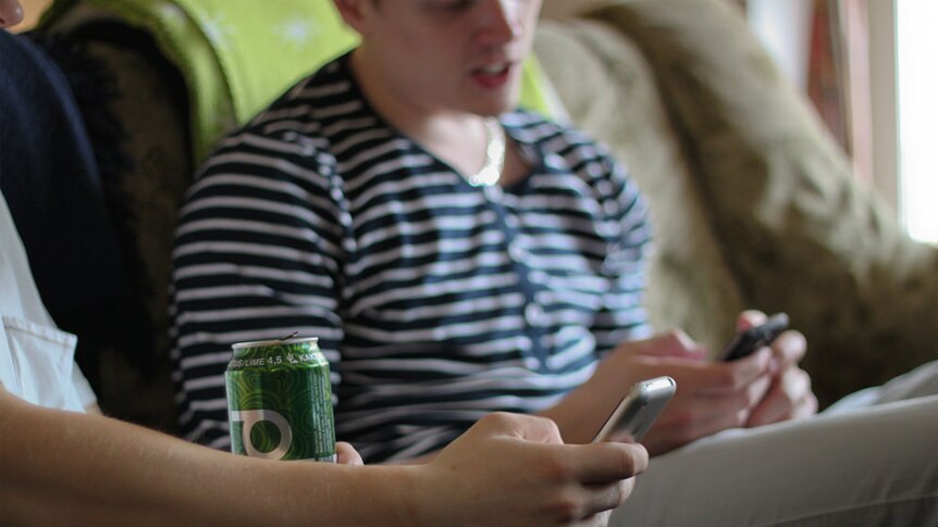 Two teenage boys sit on the couch, using mobile phones.