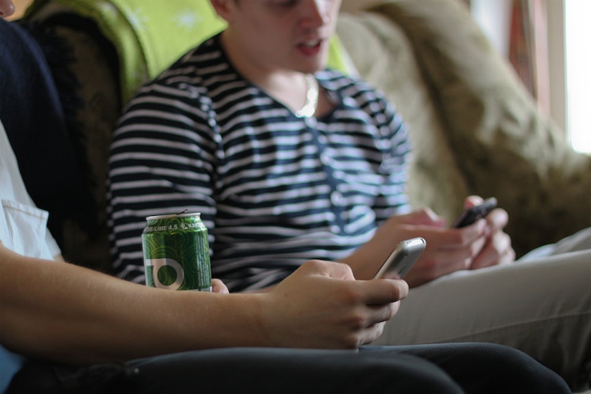 Two teenage boys sit on the couch, using mobile phones.