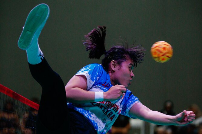 Female sepak takraw player mid-air spike towards other team.