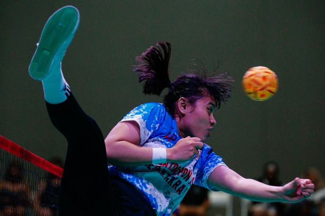 Female sepak takraw player mid-air spike towards other team.
