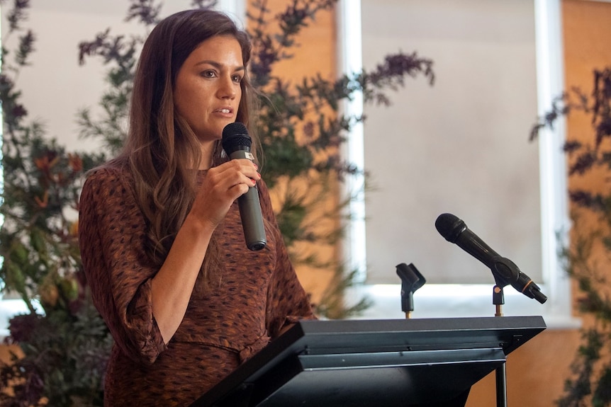 An Aboriginal woman with long black hair, holding a microphone.