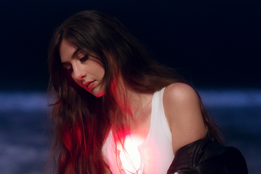 Weyes Blood looks down. She wears a white top and has long dark hair.
