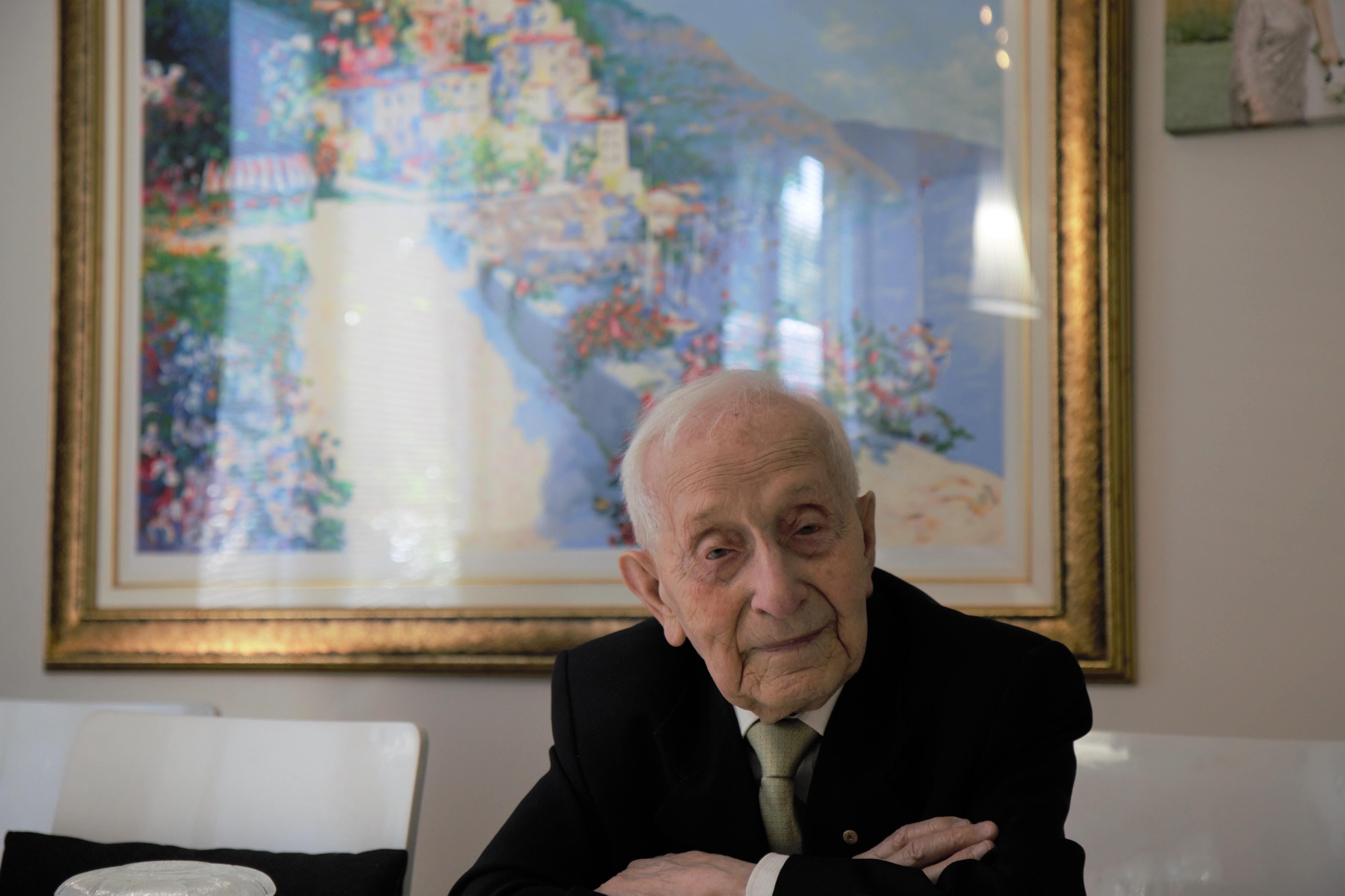 Close-up photo of Abram Goldberg in suit and tie, leaning folded arms across a table, smiling very slightly.