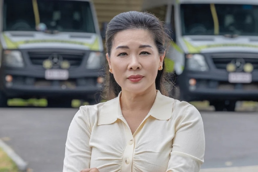 A woman standing with her arms crossed standing in front of two ambulances. 