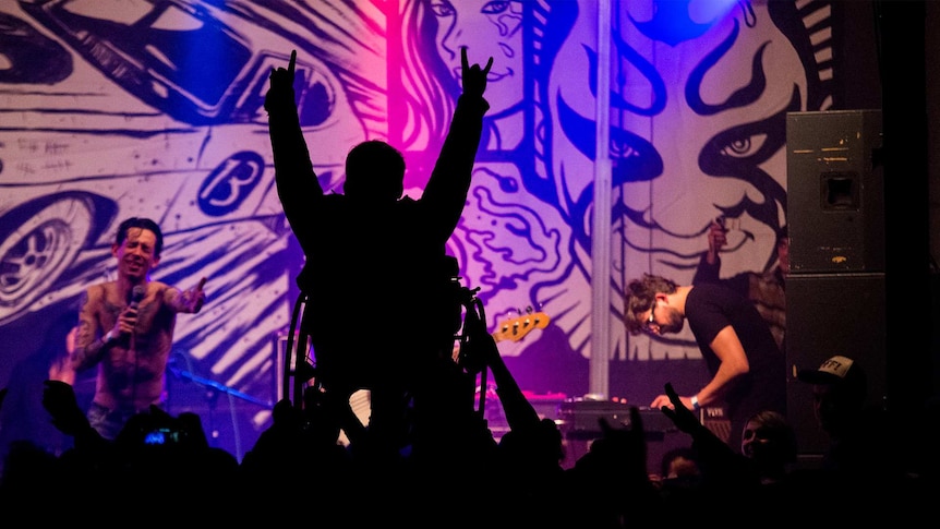 A man in a wheelchair crowdsurfs at a live music show