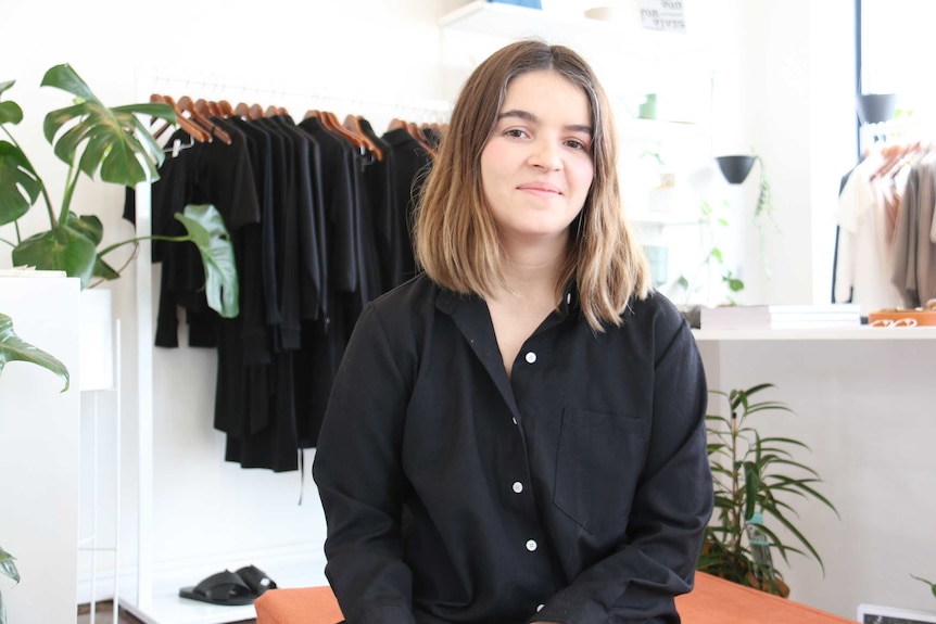 Adelaide fashion designer Anny Duff in front of a row of clothing.