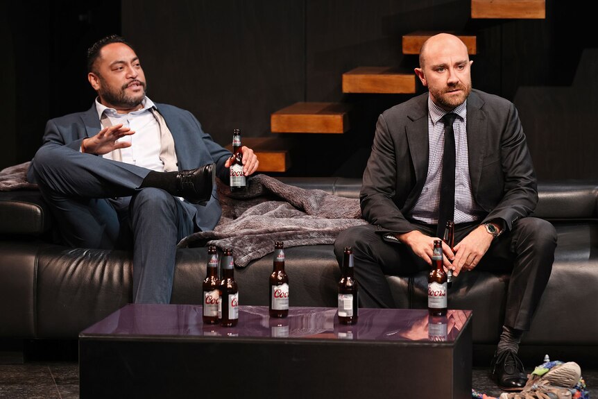 Anthony Taufa and Josh McConville in Triple X. They sit on a couch with several bottles of Coors on a table in front of them.