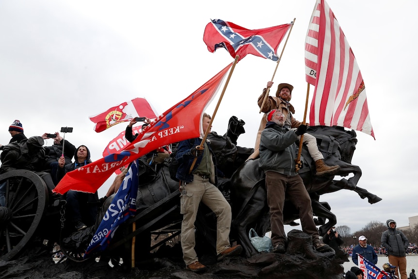 Pro-Trump protesters wave banners and a Confederate battle flag as they climb a statue.