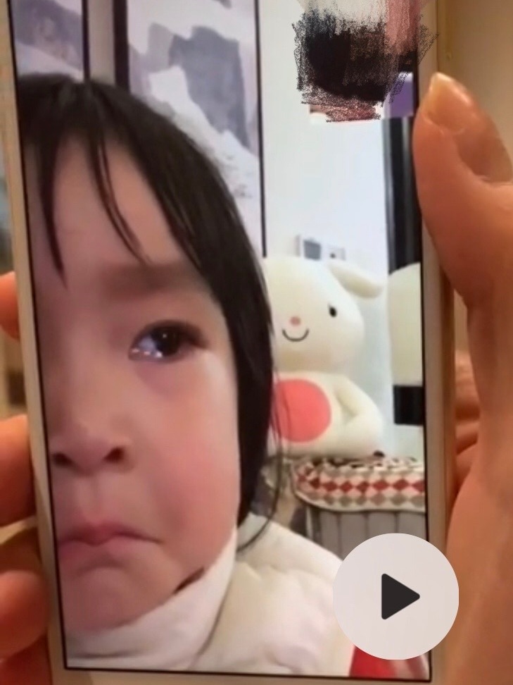 You view a portrait image of a hand holding a smartphone carrying a video of a baby with tears in her eyes.