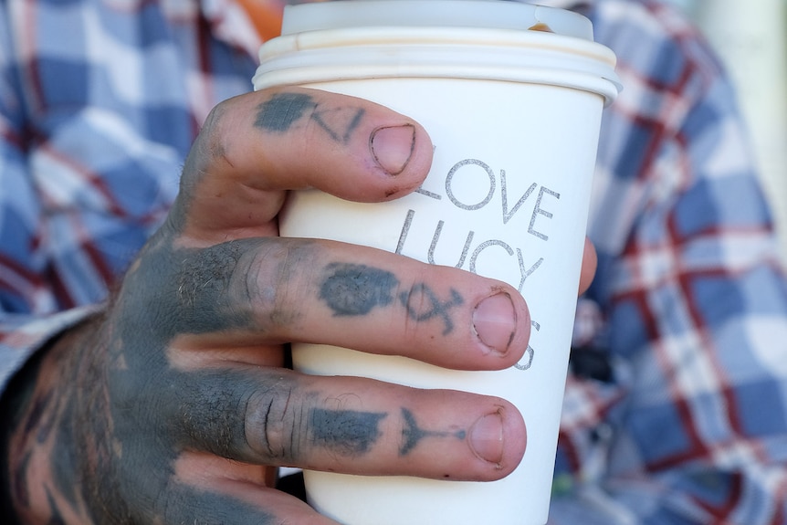 A tattooed man holds a coffee cup that reads "Love Lucy Boots". 