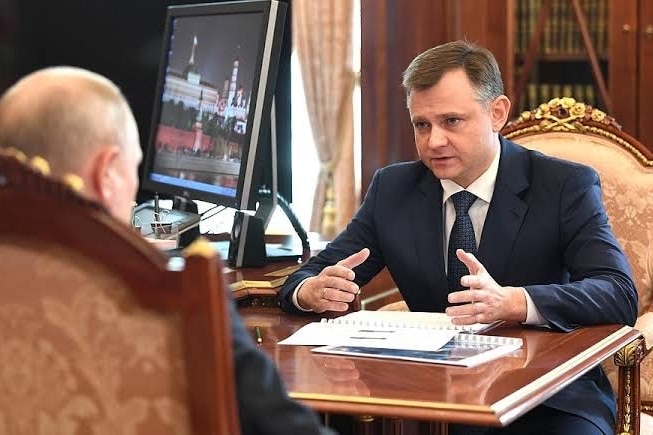Yury Slyusar wears a suit and tie and sits across from Vladimir Putin, having a conversation