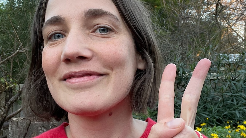 A woman in a red sweater smiles as she gives a peace sign