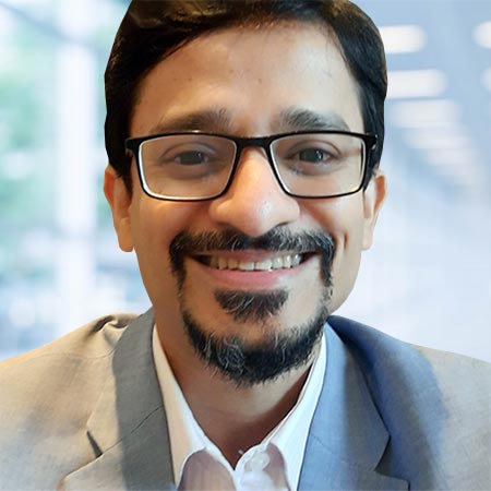 A man wearing glasses and a suit smiles at the camera