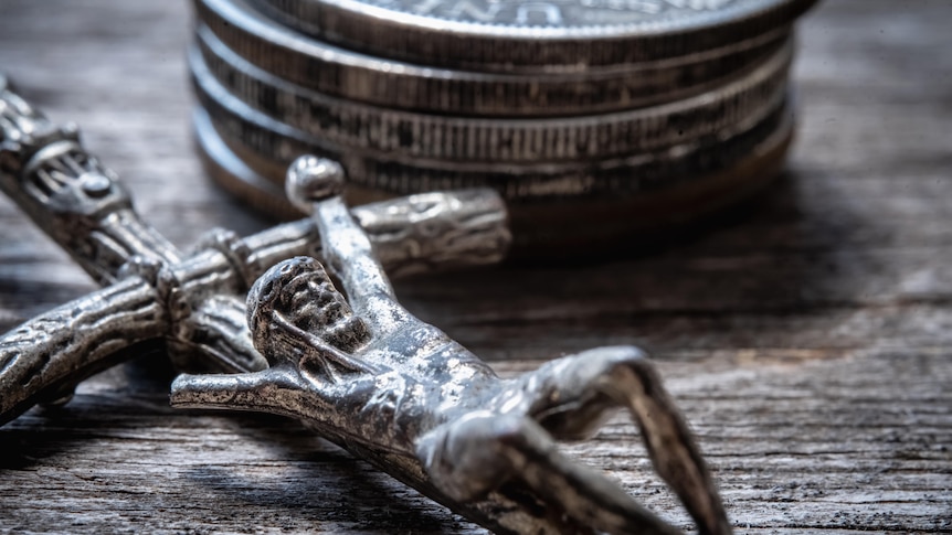 A silver crucifix with a stack of coins in the background