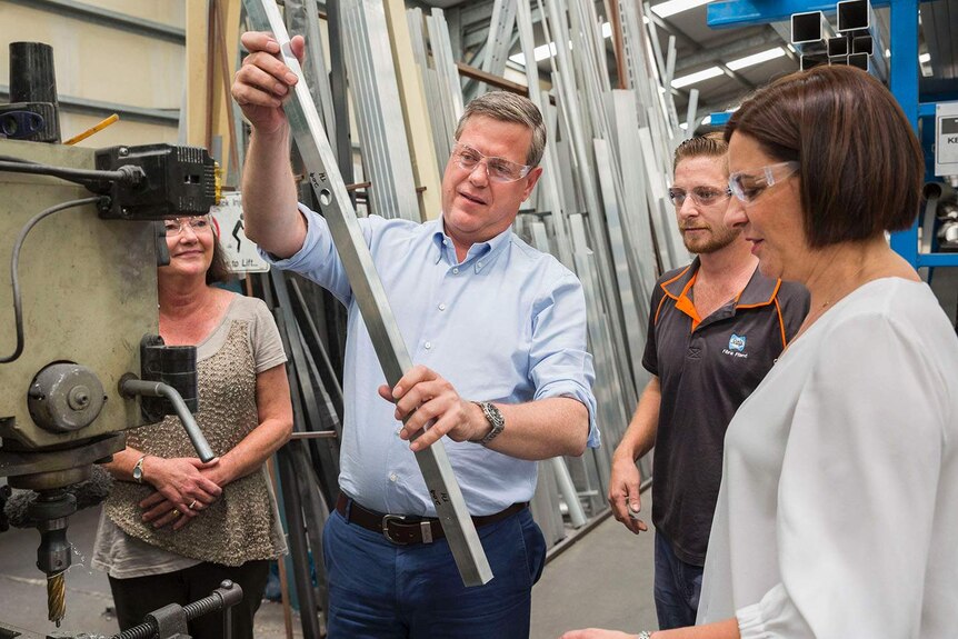 LNP leader Tim Nicholls holds and looks at a metal bar while wearing safety glasses at a Brisbane business.