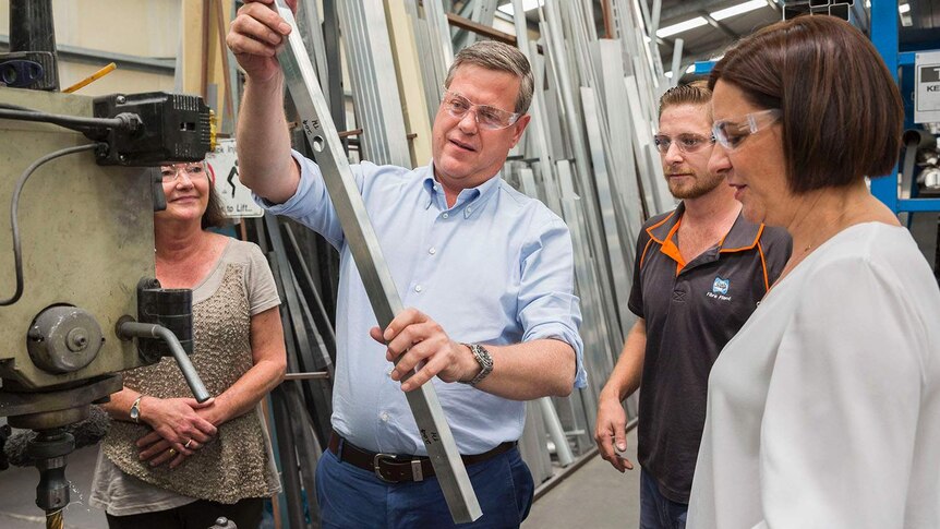 LNP leader Tim Nicholls holds and looks at a metal bar while wearing safety glasses at a Brisbane business.
