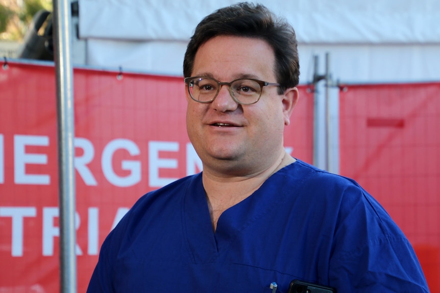 A surgeon in a blue coat speaks to the media