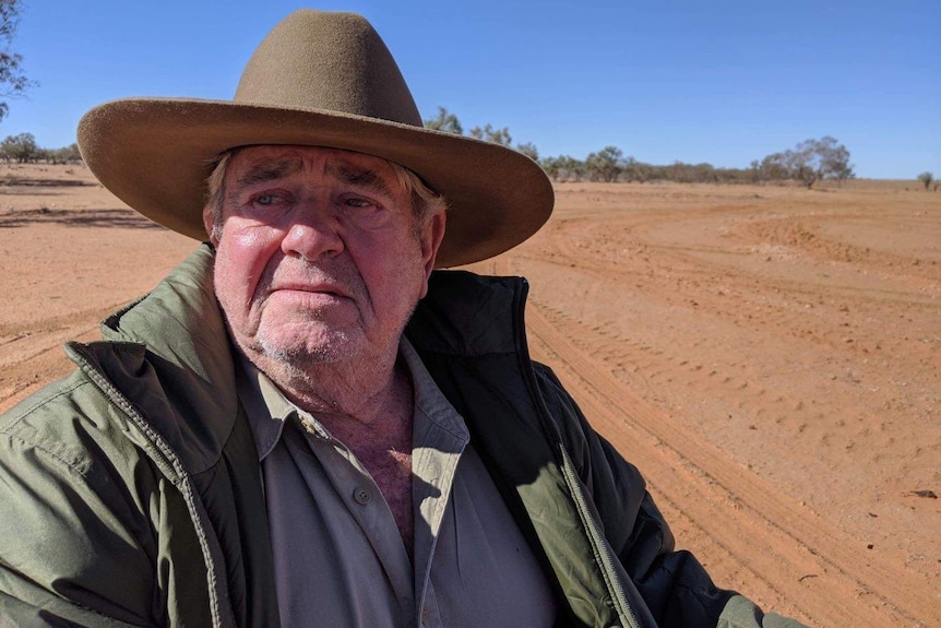 Man with a wide-brimmed hat and coat with dusty, dry landscape behind him