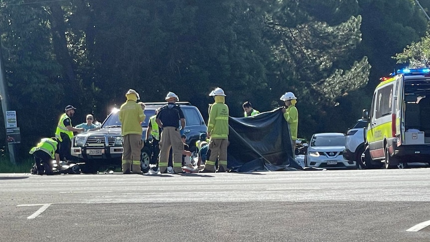 police and paramedics standing with a tarp next to a car and a motorcycle after a fatal traffic crash