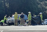 police and paramedics standing with a tarp next to a car and a motorcycle after a fatal traffic crash