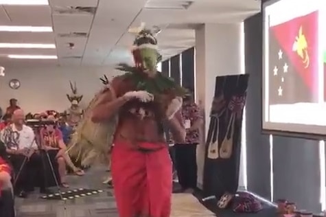 Exxon Mobil employee performs Tolai dance in red skirt with brown paint.