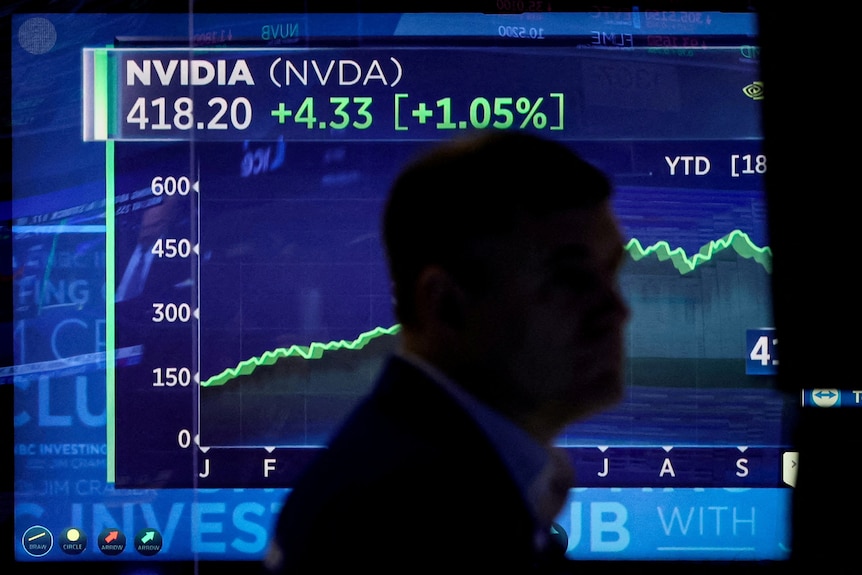 一名男子的剪影走过一块蓝色屏幕，屏幕上显示着一条逐渐上升的绿线，追踪着股票价格。