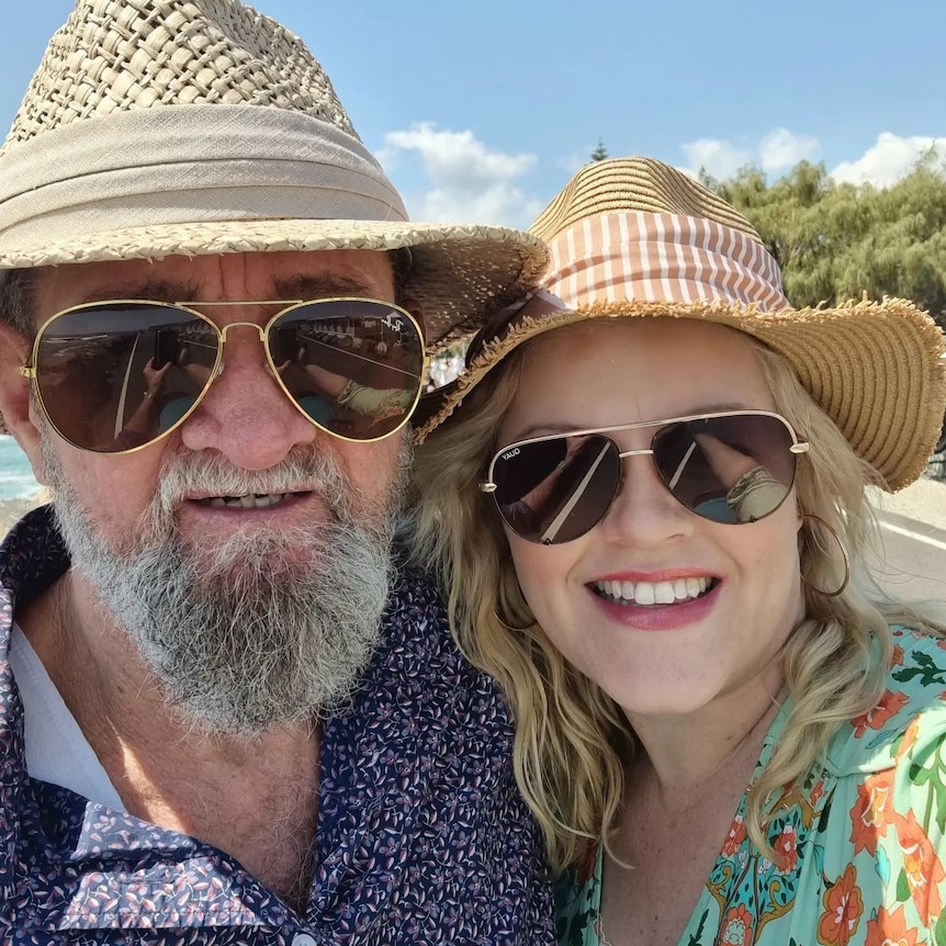 Catherine and Gregory smiling, wearing straw beach hats and glasses.