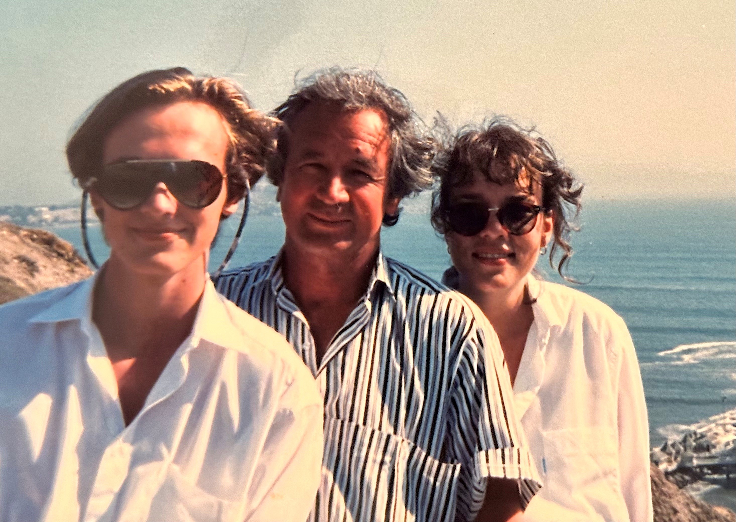 Um homem mais velho com um homem mais jovem à esquerda e uma jovem à direita.