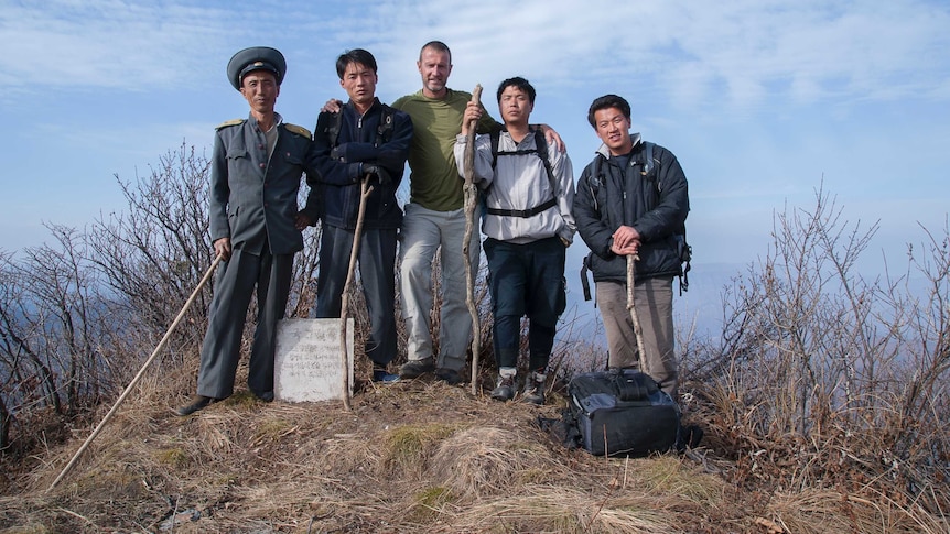 Roger Shepherd poses with four Asian men on top of a mountain.