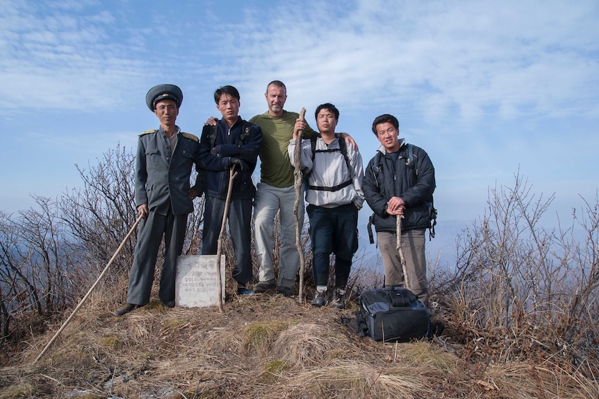 Roger Shepherd poses with four Asian men on top of a mountain.