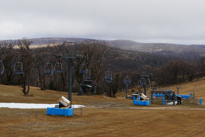 a hill with a patch of snow and a chairlift, in the background are burnt hills