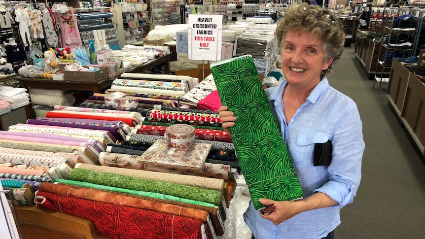 Woman holds up bolt of green fabric in country department store.