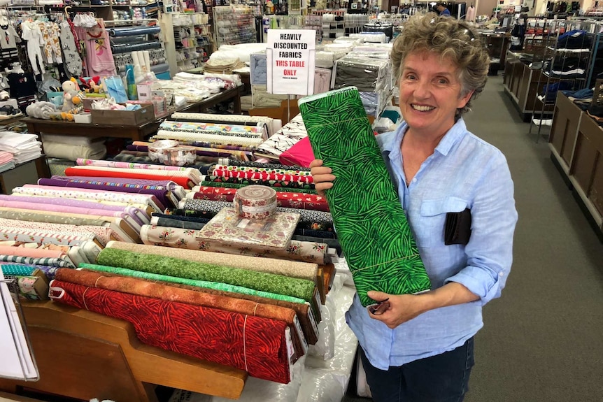 Woman holds up bolt of green fabric in country department store.