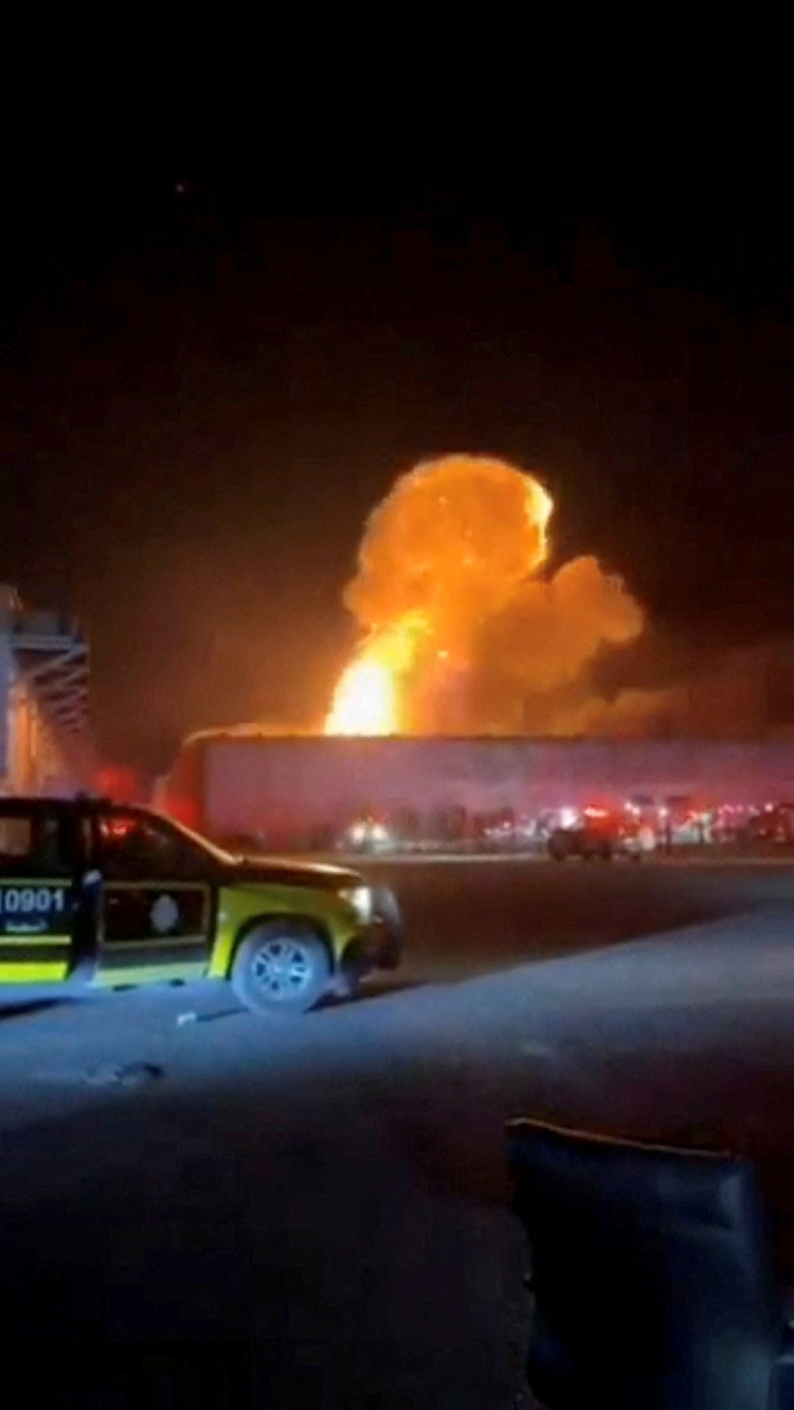 Smoke rises from an explosion with an emergency vehicle in the foregorund.
