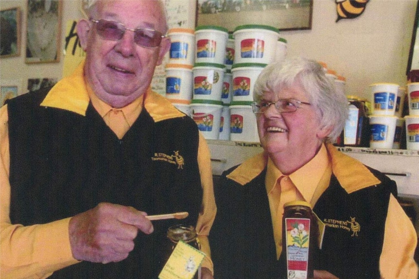 A pair of elderly people are looking are holding bottle of honey smiling