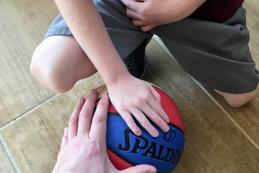 A close-up photo of a child's hand and a man's hand on a basketball on the ground.