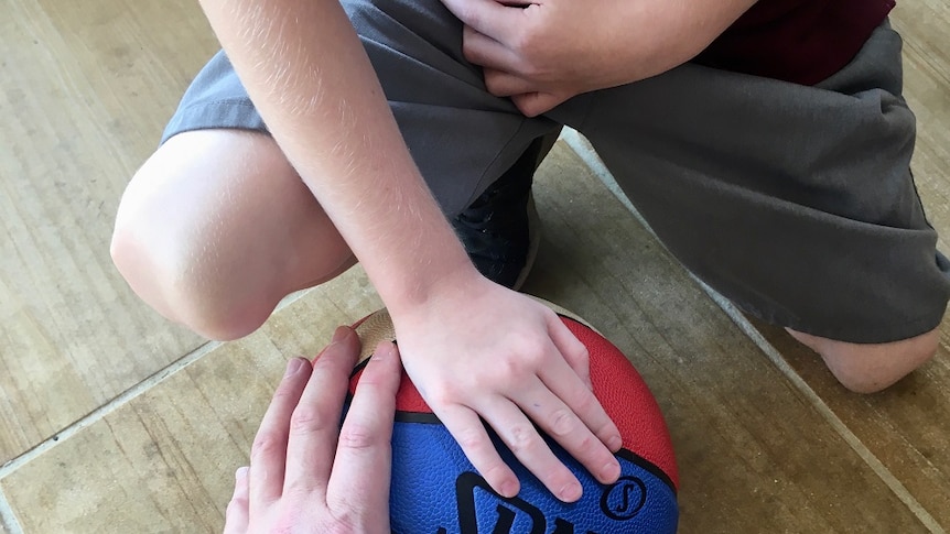 A close-up photo of a child's hand and a man's hand on a basketball on the ground.