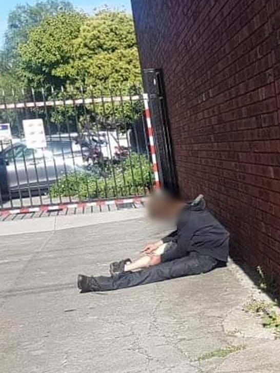 Un homme vêtu de vêtements noirs et déshabillés s'est effondré contre un mur de briques, tenant ce qui semble être une aiguille près de sa jambe.
