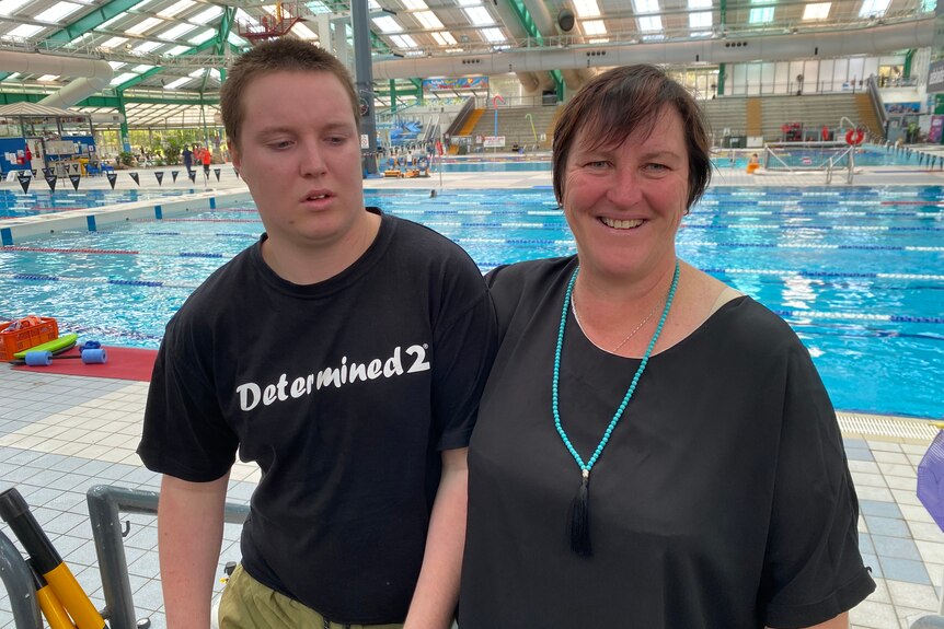 A teenager next to his mother at a swimming pool complext.