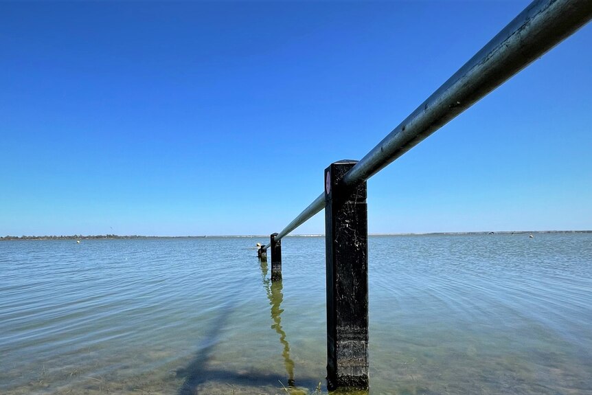 Blue water and blue skies at Lake Bonney. There is a piece of infrastructure like a rail going into the lake.