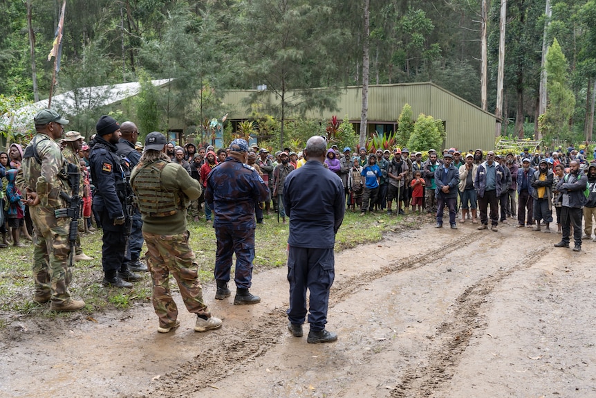 Police officials and defence personnel speaking to a crowd of people in a village.