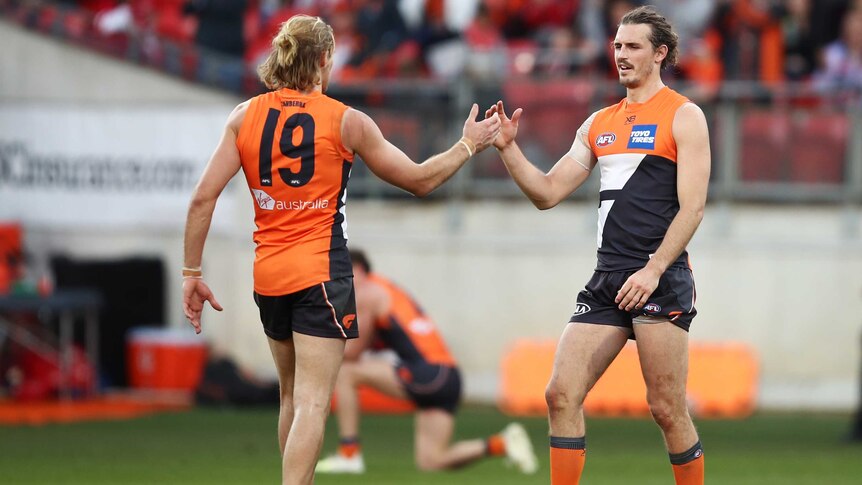 Two defenders clasp hands in celebration at the end of an AFL game in Sydney.