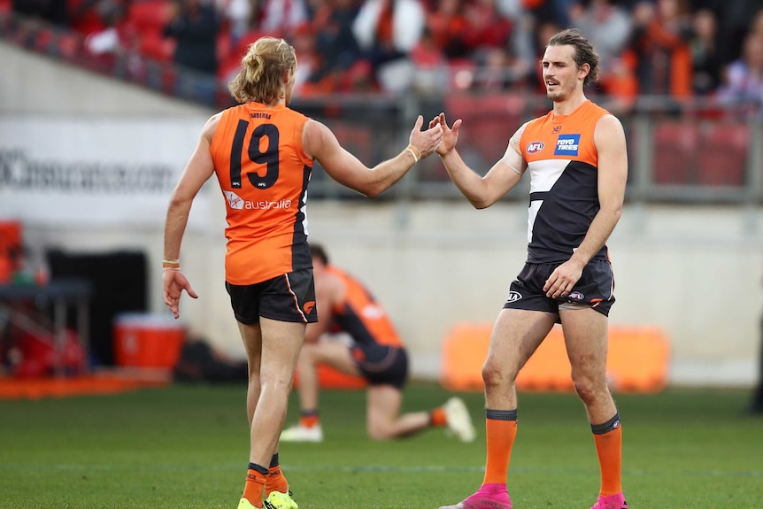 Two defenders clasp hands in celebration at the end of an AFL game in Sydney.